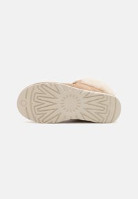 Hellbraune Schuhe mit einem weichen cremefarbenen Obermaterial aus Fell, das eine strukturierte beigefarbene Gummisohle mit geometrischem Muster zeigt.