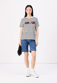 T-shirt às riscas em branco e preto com "AM♥UR" em bordô, combinado com calções de ganga azuis. Usado com ténis brancos e uma mala preta.