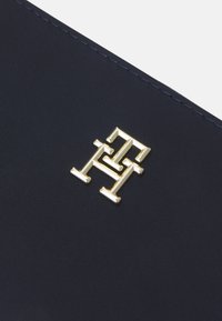 Navy fabric wallet featuring a gold geometric logo. Textured surface with sleek stitching and distinct metallic accents. Compact design.