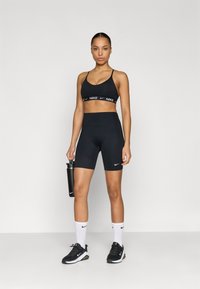 Μαύρο αθλητικό σουτιέν με λευκό λογότυπο Nike, μαύρο σορτς με ψηλή μέση, μαύρα αθλητικά παπούτσια και μαύρο παγούρι νερού. Λευκές κάλτσες με λογότυπο Nike.