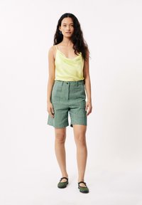 Groene gestreepte hoog-waist shorts met frontzakken, gecombineerd met een zacht gele satijnen camisoletop. Zwarte en groene schoenen maken de look compleet.