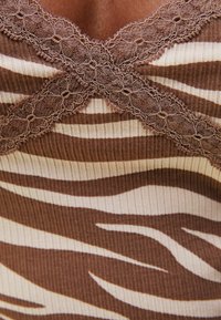 Top senza maniche marrone con texture a coste, caratterizzato da un motivo a strisce zebra in marrone chiaro e scuro, decorato con dettagli in pizzo floreale sul colletto.