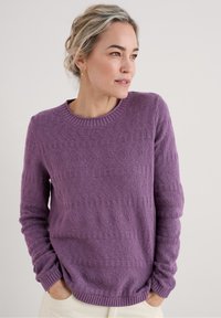 Lila stickad tröja med ett texturerat mönster, med rund halsringning och ribbade ärmslut och nederkant. Tyget verkar mjukt och andningsbart.