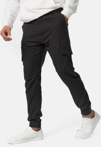 Pantalones cargo negros con tobillos ajustados, hechos de una tela texturizada, con bolsillos laterales y una cinturilla elástica, combinados con zapatillas blancas.