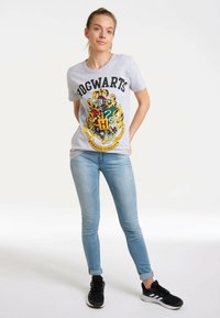 Grey cotton T-shirt with "HOGWARTS" text and colorful Gryffindor crest design. Paired with light blue skinny jeans and black sneakers.