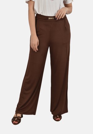 Pantaloni marroni a gamba larga con una fibbia dorata decorativa in vita, indossati con sandali scuri aperti e un top bianco.