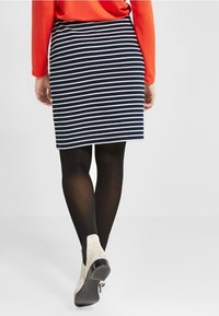 Striped pencil skirt in navy and white, featuring a fitted design. Worn with black tights and light-colored ankle boots.