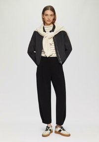 Zwarte cropped bomberjack, gestreepte wit en beige trui, zwarte tapered broek en beige sneakers met zwarte accenten en een bruine zool.