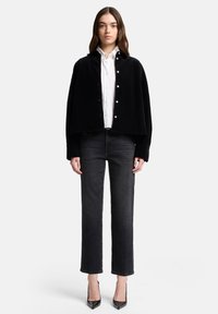 Czarna welurowa krótka kurtka zapinana na guziki, noszona na białej koszuli zapinanej na guziki. Do tego ciemne jeansy o prostych nogawkach i czarne szpiczaste szpilki.