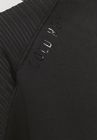Haut de sport noir avec un design texturé, des accents côtelés et un logo brillant "COLD.RDY" sur le côté.