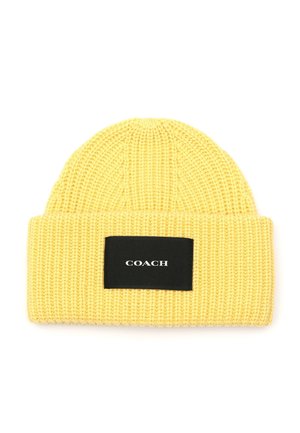 Bonnet jaune en tricot avec un revers et un patch rectangulaire noir affichant le mot "COACH" en lettres blanches.