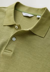 Világoszöld kötött galléros póló bordázott gallérral, két fehér gombbal, és a méretcímkéjén "NEXT Medium Regular Fit" felirattal.