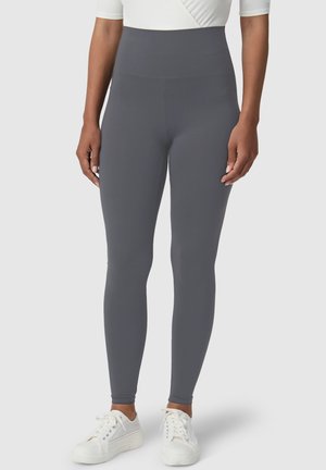 Szare legginsy z wysokim stanem wykonane z elastycznego materiału, charakteryzujące się gładką fakturą i dopasowanym krojem, zestawione z białymi trampkami.