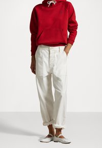 Felpa rossa con tasca a marsupio, pantaloni bianchi larghi e ballerine bianche con dettagli in nastro. Tessuto casual e maniche risvoltabili.