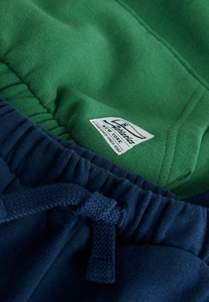 Grüne und marineblaue Sweatpants bestehen aus einem weichen Baumwollmischgewebe, haben einen elastischen Bund mit Kordelzug und ein Etikett, das im Innenfutter eingestickt ist.