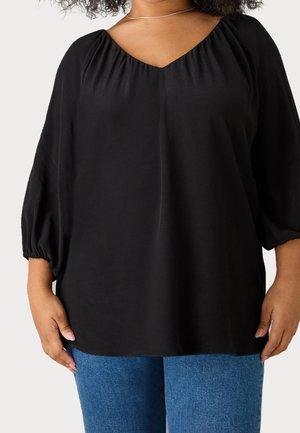 Blusa nera con scollatura a V e spalle arricciate. Presenta maniche ampie a palloncino e un tessuto morbido e leggero. Abbinata a jeans blu.