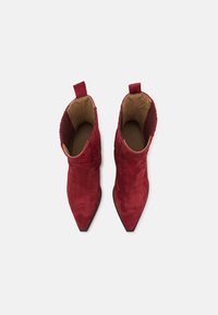 Rote Wildleder-Stiefeletten mit spitzen Zehen, dekorativen Nähten und Schlaufen. Strukturiertes Detail im oberen Bereich und kontrastierendes hellbraunes Innenfutter.