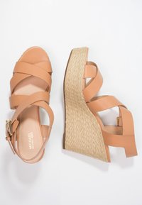 Sandalias de cuña de cuero marrón con tiras entrelazadas, tacón envuelto en yute y una plantilla ligeramente texturizada. Cierre con hebilla ajustable en el lateral.
