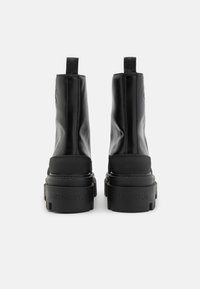 Bottines noires en cuir synthétique lisse, avec une semelle épaisse et un logo détaillant sur le talon, dotées de languettes pour un enfilage facile.