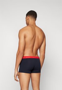 Tengerészkék pamut boxer shorts piros derékrésszel, rajta a "TOMMY HILFIGER" logóval; sima textúra, testhez simuló fazon és közepes magas derék.