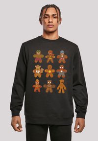 Melna sporta krekls ar krāsainām piparkūku stila supervaroņu figūrām, kas sakārtotas trīs rindās. Dizainā ir iekļauti dažādi supervaroņu motīvi un detaļas.