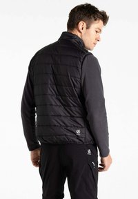 Black puffer vest with quilted design, high collar, and logo detail at the hem, worn over a long-sleeved dark top.