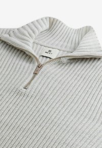 Un pull en laine grise clair avec un col côtelé et une fermeture éclair demi-zip ; présente un motif de points texturé et une étiquette de marque sur le col.