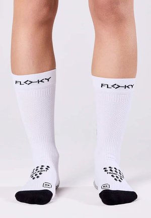 Weiße Sportsocken mit schwarzem Branding am oberen Bündchen, ausgestattet mit gummierten Grip-Mustern an den Sohlen, die zur Orientierung gekennzeichnet sind.
