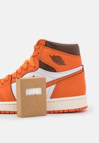 Oranžové kožené vysoké tenisky s bílými a hnědými detaily, s texturovanou podrážkou. Součástí je krabice na boty s bílými tkaničkami.