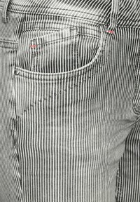 Jean rayé noir et blanc avec un gros plan sur la poche arrière, présentant des coutures rouges. La texture est lisse avec des détails de couture visibles.