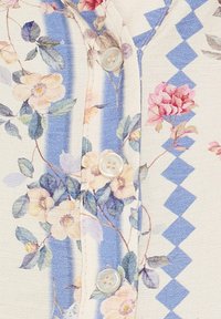 Bluse med blomsterprint i cremefarve med blå striber og zigzag-detaljer. Har runde knapper, letvægtsstof og teksturerede stingdetaljer.