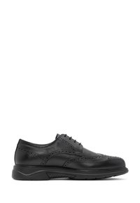 Chaussure brogue en cuir noir avec un design à bout « gibier », des détails perforés et une semelle en caoutchouc noir, présentée en profil latéral.
