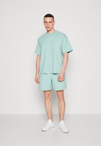 Set de tricou și pantaloni scurți verde menta, realizat dintr-un material moale, cu mâneci scurte și croială lejeră. Asortat cu adidași albi.