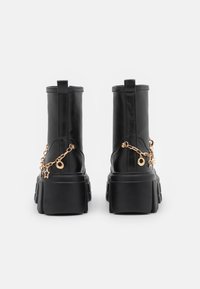 Mustat nahkaiset nilkkurit, joissa on paksu pohja, kultaketju korostuksilla ja tähtimuotoisilla riipuksilla sivuilla.