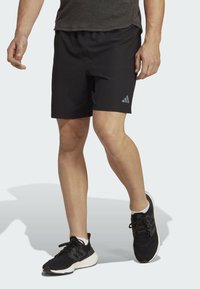 Pantalones cortos deportivos negros con una cinturilla elástica y un pequeño logo gris en la pierna izquierda. Combinados con zapatillas deportivas negras y calcetines blancos.