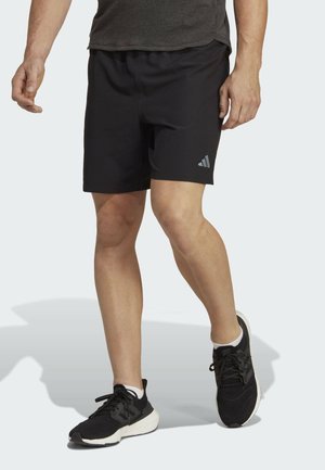Pantalones cortos deportivos negros con una cinturilla elástica y un pequeño logo gris en la pierna izquierda. Combinados con zapatillas deportivas negras y calcetines blancos.