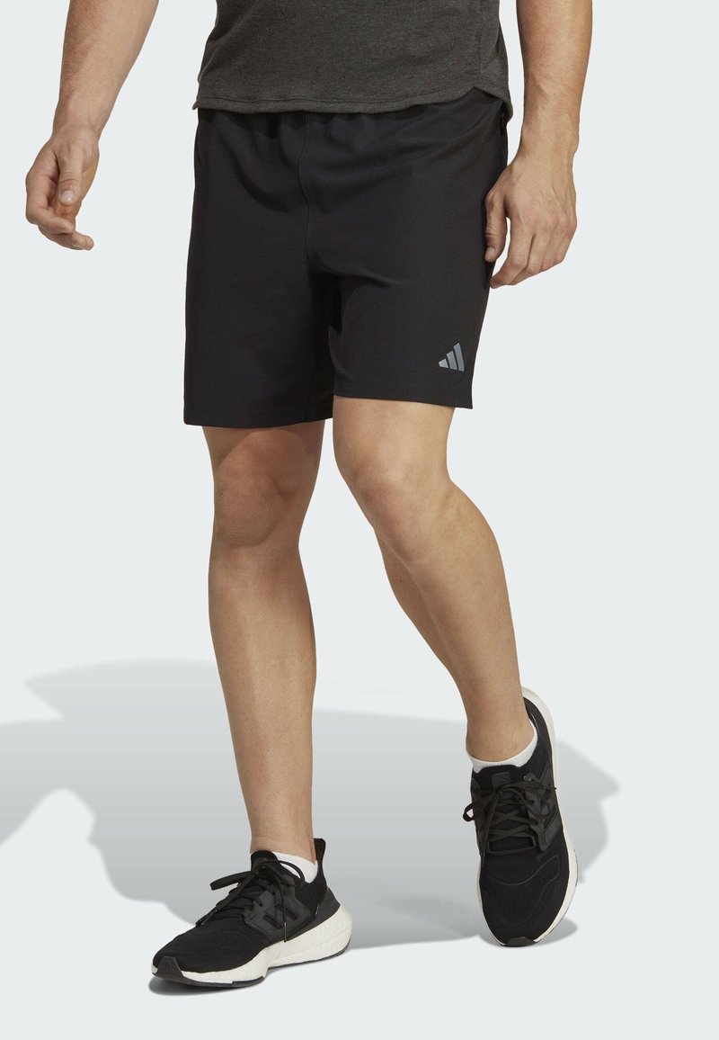 Pantalones cortos deportivos negros con una cinturilla elástica y un pequeño logo gris en la pierna izquierda. Combinados con zapatillas deportivas negras y calcetines blancos.