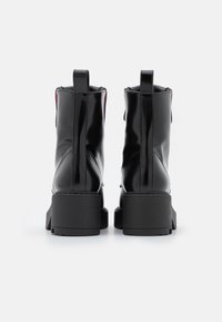 Schwarze Ankle-Boots aus Lackleder mit einer klobigen, strukturierten Sohle und Zuglaschen hinten, mit kontrastierenden Details des inneren Futters.