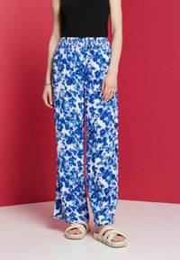 Flödande, vida byxor i vitt tyg med ett blått blommönster. Har en elastisk midja och en mjuk textur, i en kombination med lätta sandaler.
