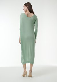 Vestido largo de color verde menta con una tela ligera, diseño de espalda en V y mangas largas. Combinado con zapatos de tacón nude.