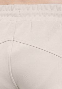 Lys beige leggings med elastisk talje, glat tekstur og skrå sømdetaljer på ryggen. Stoffet ser strækbart ud.