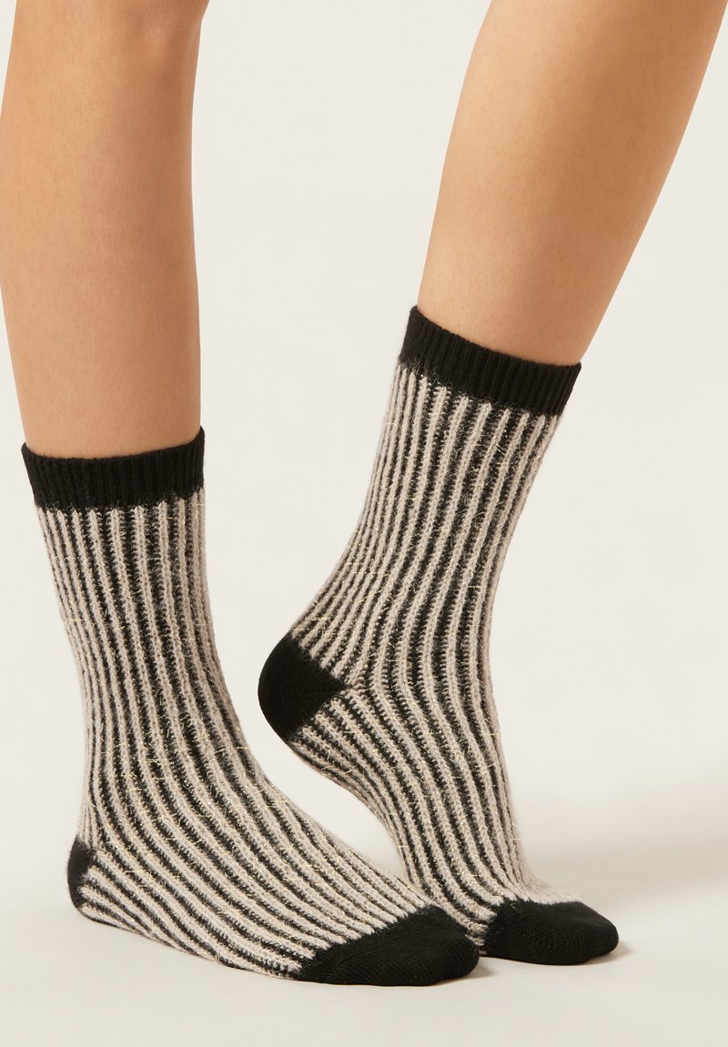 Feet wearing black and white vertically striped wool socks with black cuffs, heels, and toes against a plain light background.