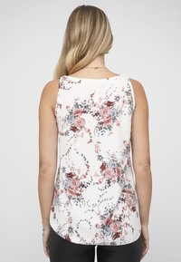 Mouwloze top met bloemenpatroon in het wit, met roze en blauwe bloemen en groene bladeren. Gladde stof met een afgeronde zoom en een ontwerp aan de achterkant.