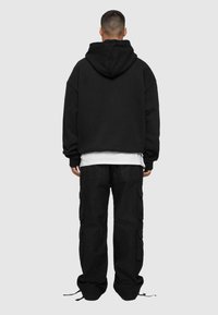 Felpa nera oversize con una grande tasca posteriore e cappuccio con cordino, abbinata a pantaloni cargo neri con più tasche laterali.