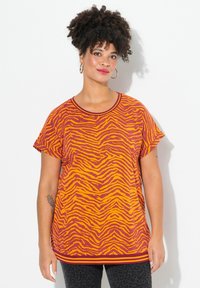 Camiseta de manga corta en color naranja con un patrón de rayas de cebra en rojo oscuro y amarillo. Presenta un escote redondo y un dobladillo acanalado.
