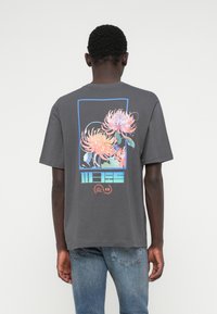 Graues Baumwoll-T-Shirt mit einer bunten Grafik von Blumen und geometrischen Formen auf der Rückseite. Rundhalsausschnitt und kurze Ärmel.
