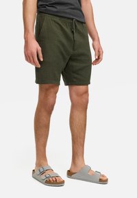 Grønne, teksturerte shorts med elastisk linning og snøring, sammen med grå sandaler med justerbare stropper og korksåler.
