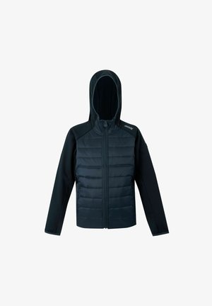 Niño de pie con las manos en los bolsillos, vistiendo una chaqueta azul oscuro, pantalones a juego y zapatos deportivos negros y verde neón.