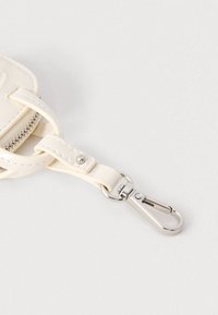 Curea de geantă din piele albă cu clemă metalică argintie în formă de carabină, pe un fundal gri deschis.