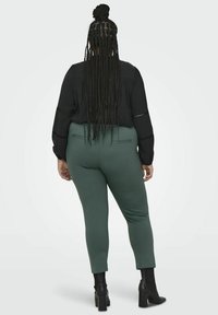 Svart bluse med lange ermer og detaljert søm på armene, kombinert med tettsittende bukser i skogsgrønt og svarte ankelstøvletter med hæl.